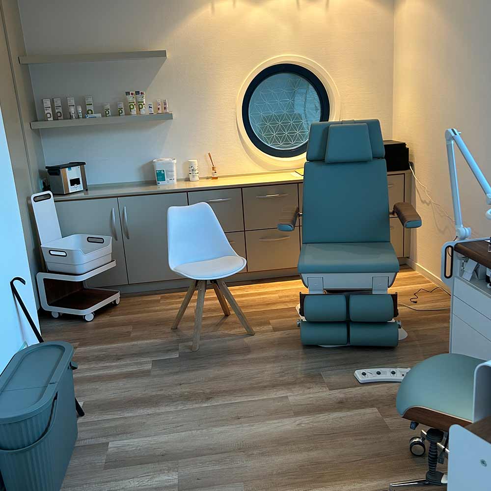 Ein modernes Behandlungszimmer mit kreisförmigem Fenster und grünem Stuhl.